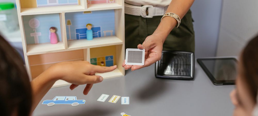 Unrecognizable teacher explaining to her students the parts of a sustainable house showing a toy solar panel