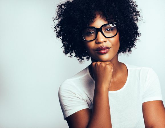 Studio portrait of serious woman in oversized glasses with her chin on her hand