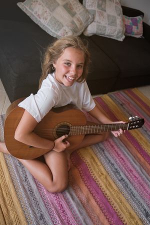 Positive kid sitting on floor and playing guitar