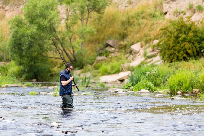 Fisherman crossing river with rod