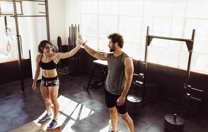 Man and woman standing on box and giving high five at gym