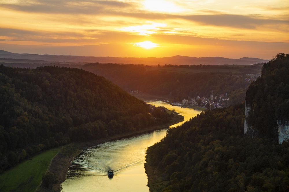 Boat on river between trees during sunset