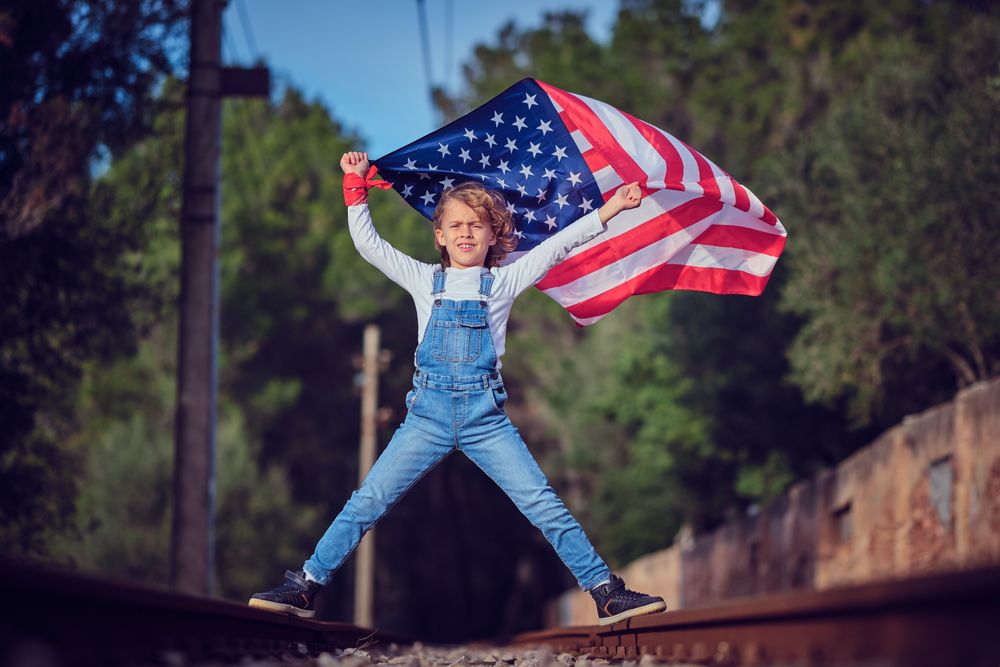Child with flag of America celebrating Independence Day on railway