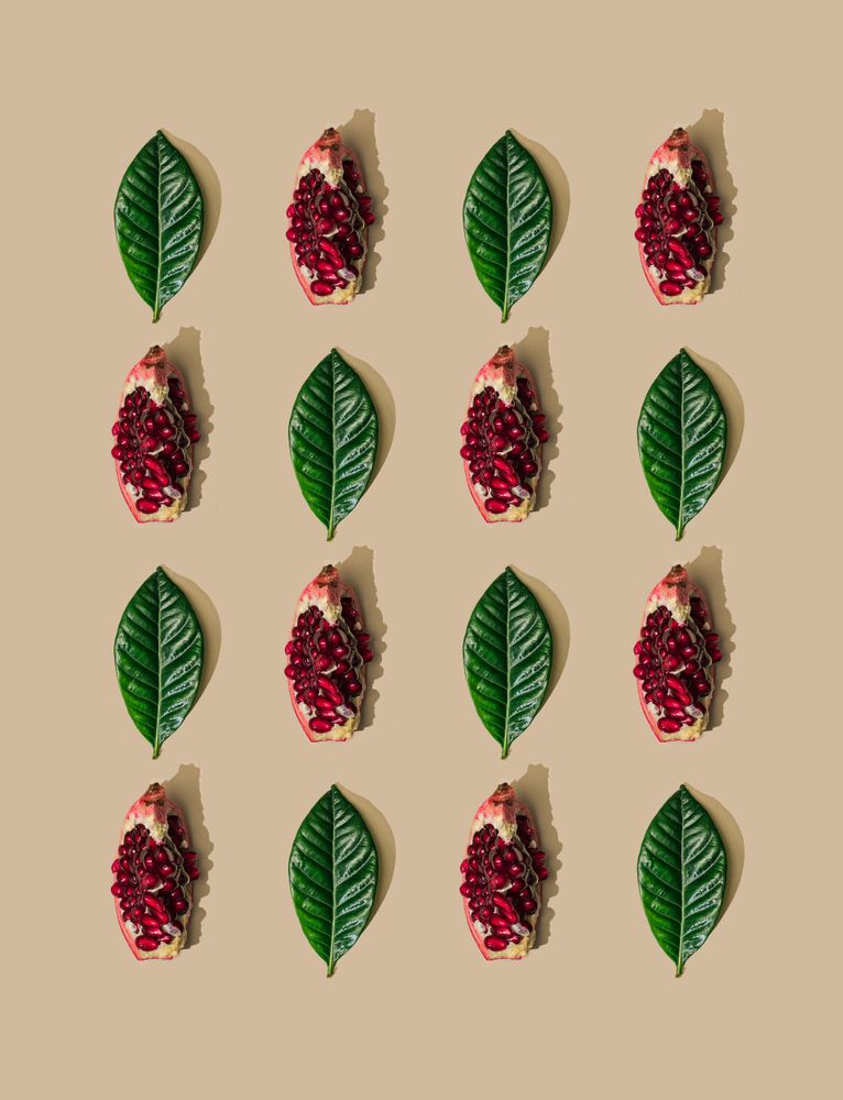 Pattern of green leaves and pomegranate slices on pastel sand background