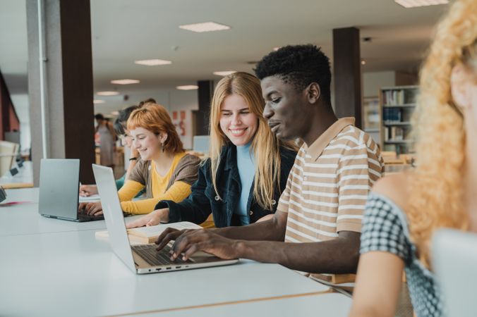 Cheerful diverse friends doing assignment using laptops in university
