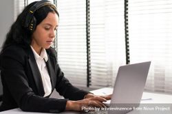 Woman wearing headphones while concentrating on typing on laptop 5Qpdg0