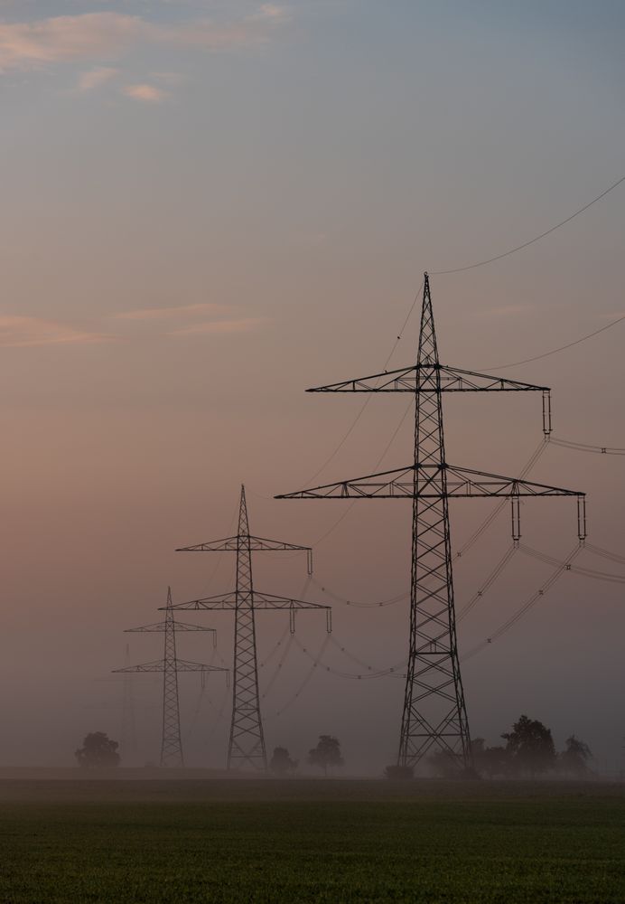 Electricity pylons in a row through fog at sunrise, in a german village