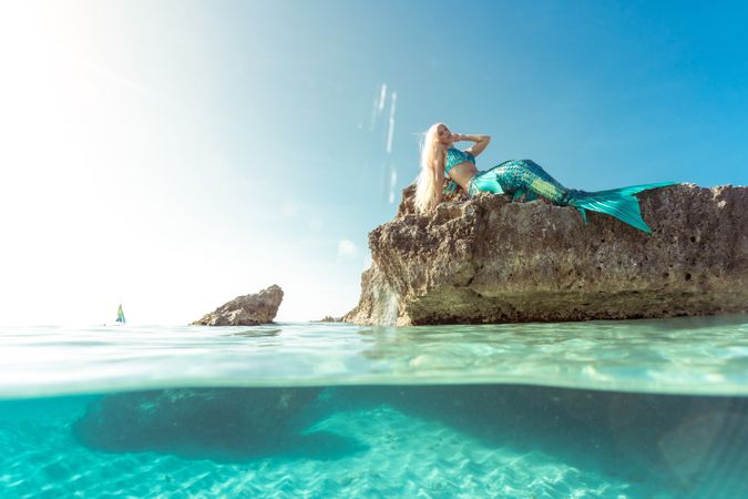 Blond fairytale female mermaid lying on rock