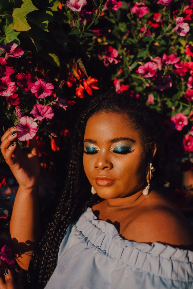 Joyful trendy Black woman standing beside blossomed tree