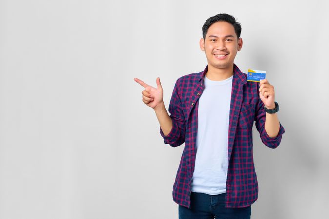 Asian male in grey studio with pointing to the side with credit card