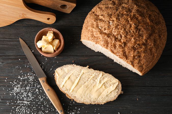 Cutting boards, bread, salt, knife and butter on wooden background, top view and space for text