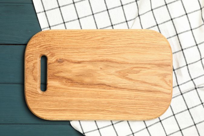 Kitchen towel with cutting board on wooden background, top view