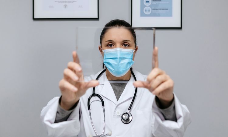 Female doctor with protective mask holding transparent tablet