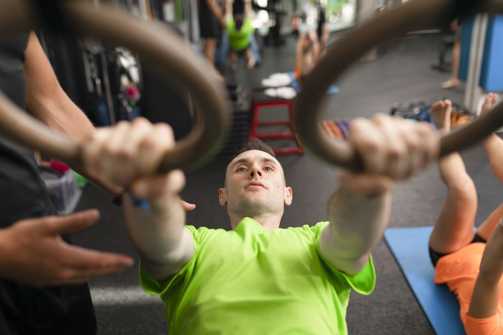 A male trainee hanging from the rings at the gym