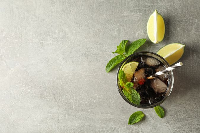 Glass with cold cola and citrus on grey table, top view