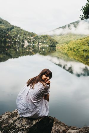 Woman sitting on rock near lake and mountains