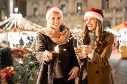 Two young women lighting a sparkler and toasting with champagne at a Christmas party.