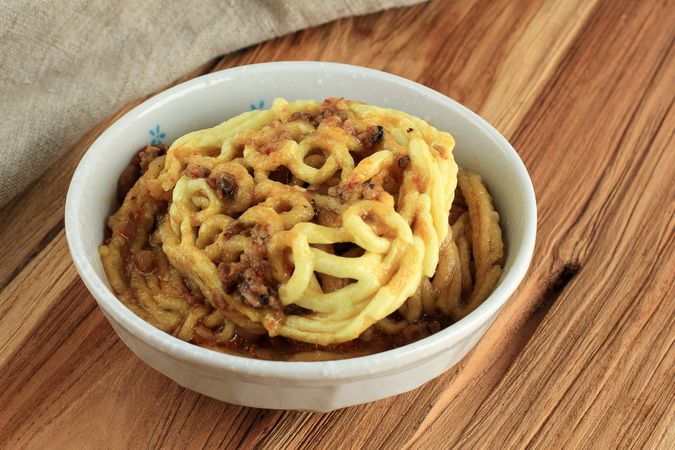 Crispy kerupuk mie banjur sambel oncom mixed with sauce in bowl served on wooden table