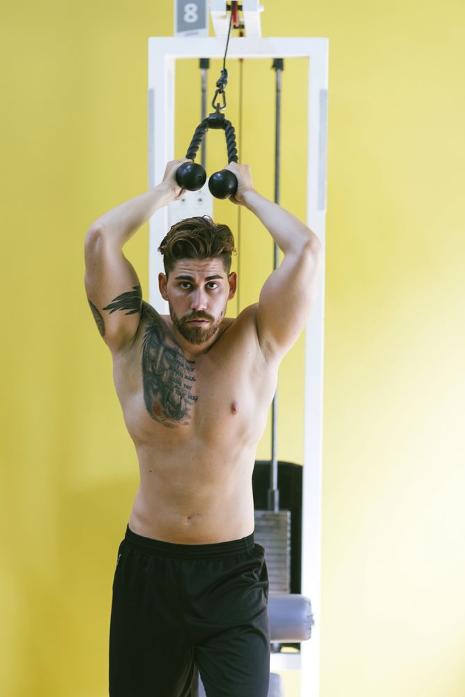 Shirtless male in gym working out his arms using weights machine
