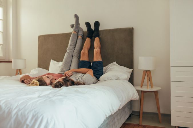 Playful couple lying on bed with legs raised to the wall and talking