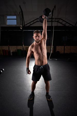 Strong sportsman doing exercises with dumbbell in gym