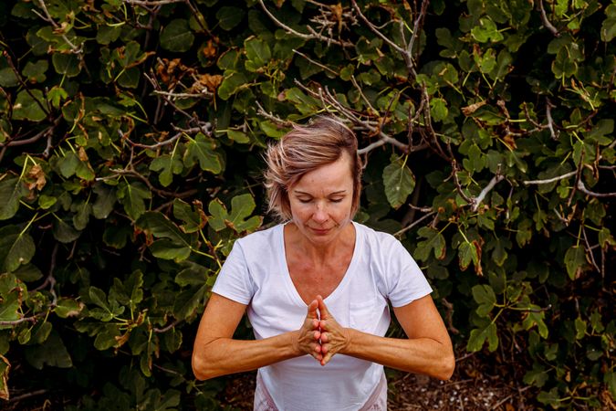 Adult woman meditating near bush