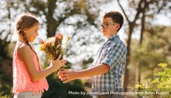 Boy giving flowers to a girl standing in a park bEkmM5