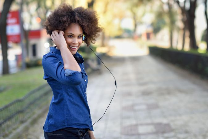 Mid shot of smiling female looking back outside in denim shirt while holding her headphones