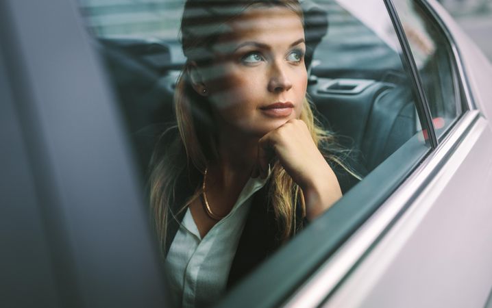 Beautiful young businesswoman sitting on back seat of a car and looking outside the window