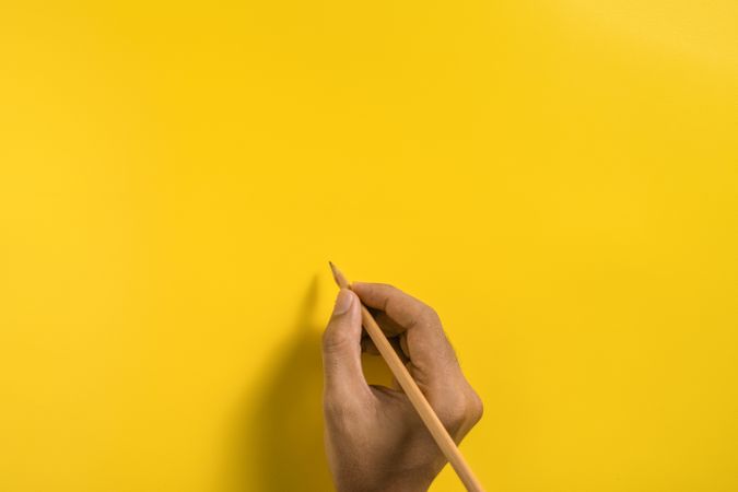 top view of male hand writing on yellow blank surface