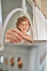Charming curly boy taking clothespins from basket for drying clo