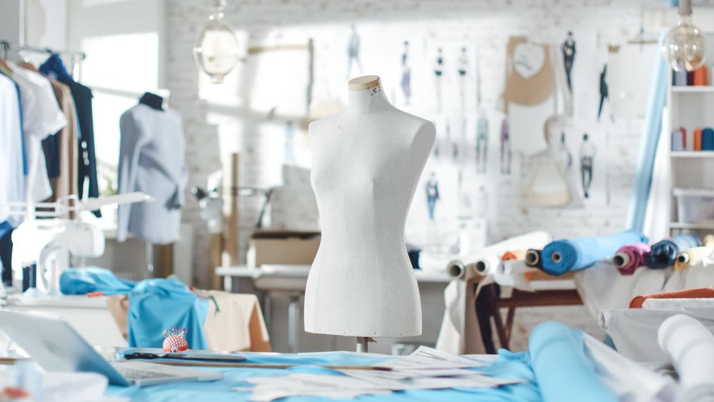 Shot of a Tailoring Mannequin that Stands in a Bright and Sunny Studio. Various Sewing Items and Colorful Fabrics