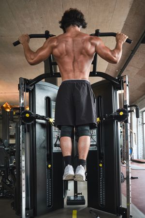 Muscular guy doing pull ups on exercise machine