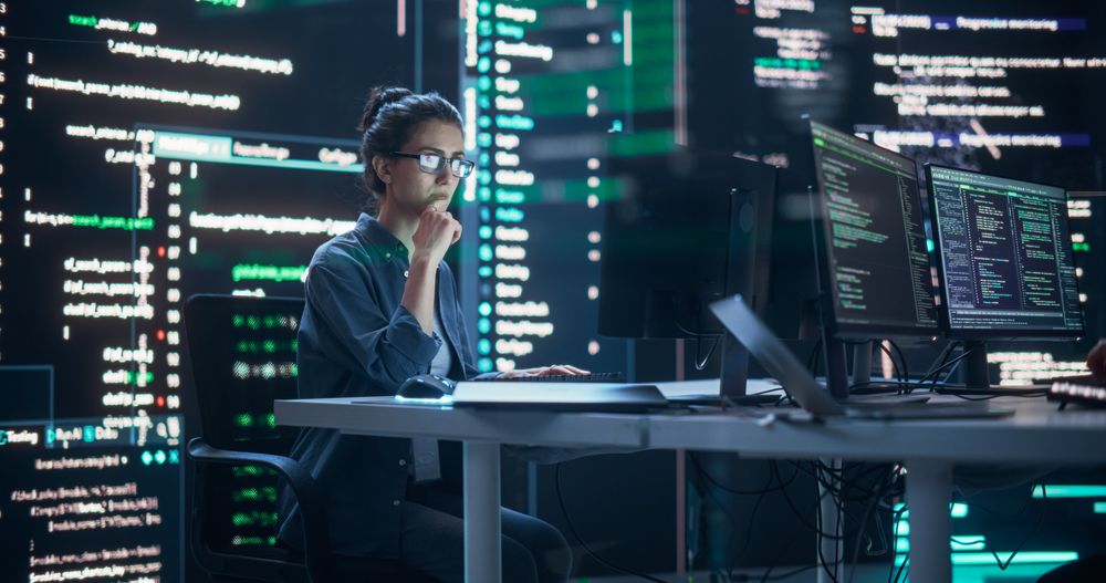 Focused Woman Working on a Computer, Typing Lines of Code that Appear on Big Screens Surrounding her in a Monitoring Room.
