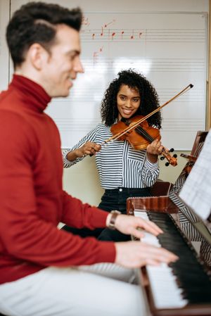 Man playing piano near woman playing violin in studio