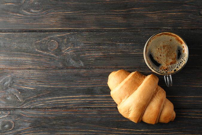 Tasty croissant with coffee on wooden background, top view and copy space