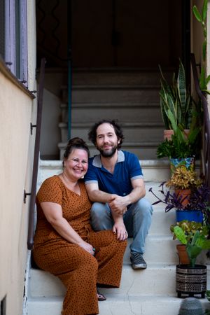 Happy partners sitting on apartment stairs outside smiling and looking at camera