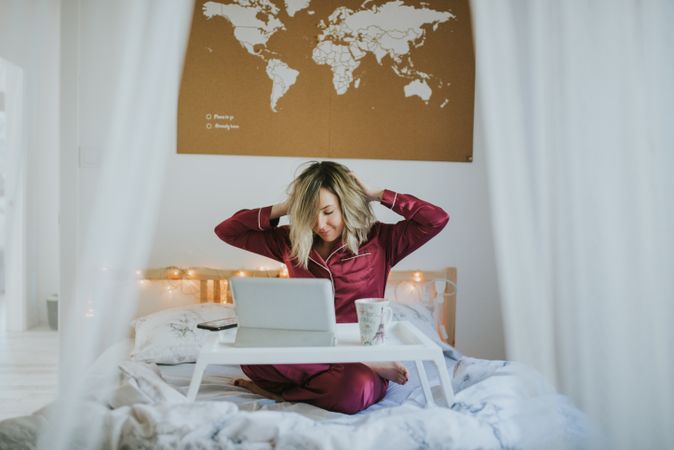Woman stretching in bed with laptop