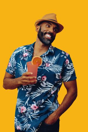 Happy male holding a cocktail while wearing colorful shirt with yellow background, vertical