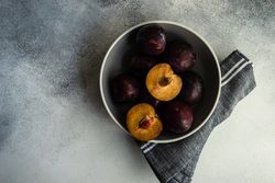 Top view of halved ripe plums in a bowl