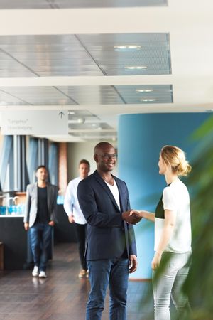 Male and female business colleagues shaking hands in busy office, vertical