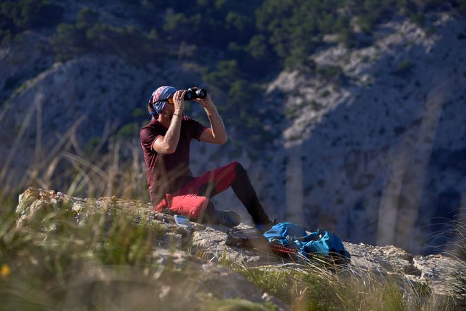 Male tourist sitting on rock with binoculars