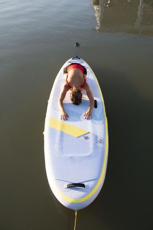 Woman in child’s pose on paddleboard on the water
