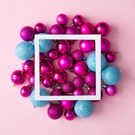 Arrangement of pink and blue festive baubles on pink background with square outline