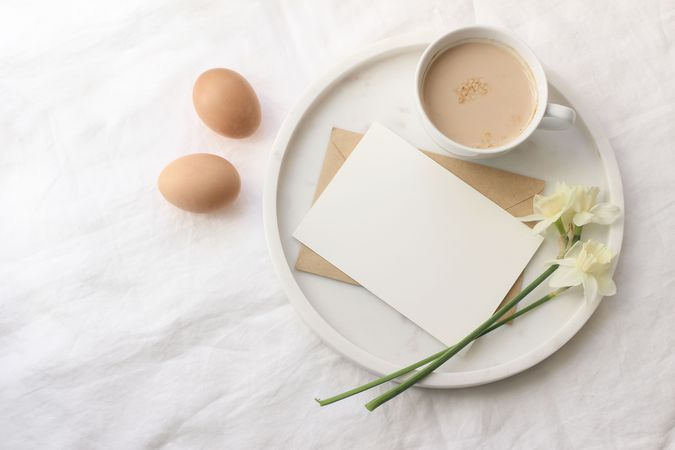Breakfast spring composition. Mug of latte coffee, bouquet of narcissus, daffodil flowers on marble tray. Blank greeting card mockup.