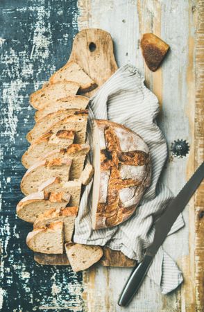 Homemade loaf with slices arranged in line with serrated knife, on wooden board with linen