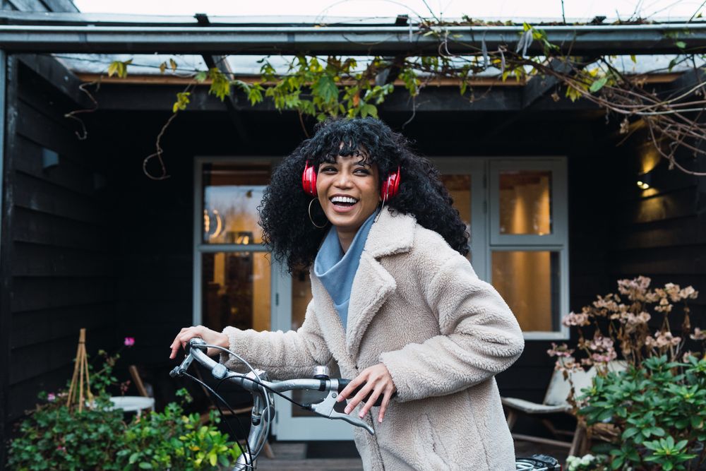 Cheerful Black woman in headphones with bicycle