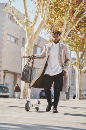 Black male walking with scooter on street