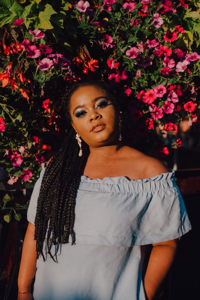 Joyful trendy Black woman standing beside blossomed tree