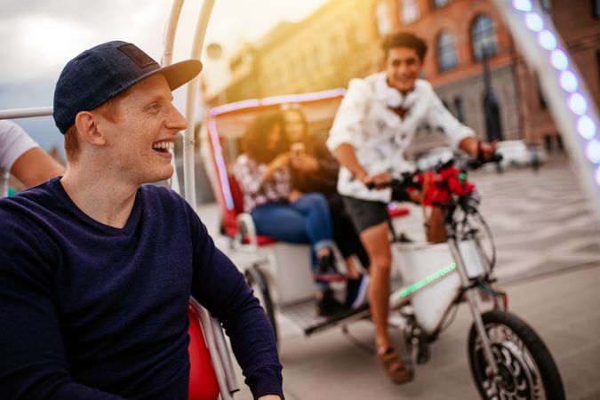 Happy young man enjoying tricycle ride in the city with friends